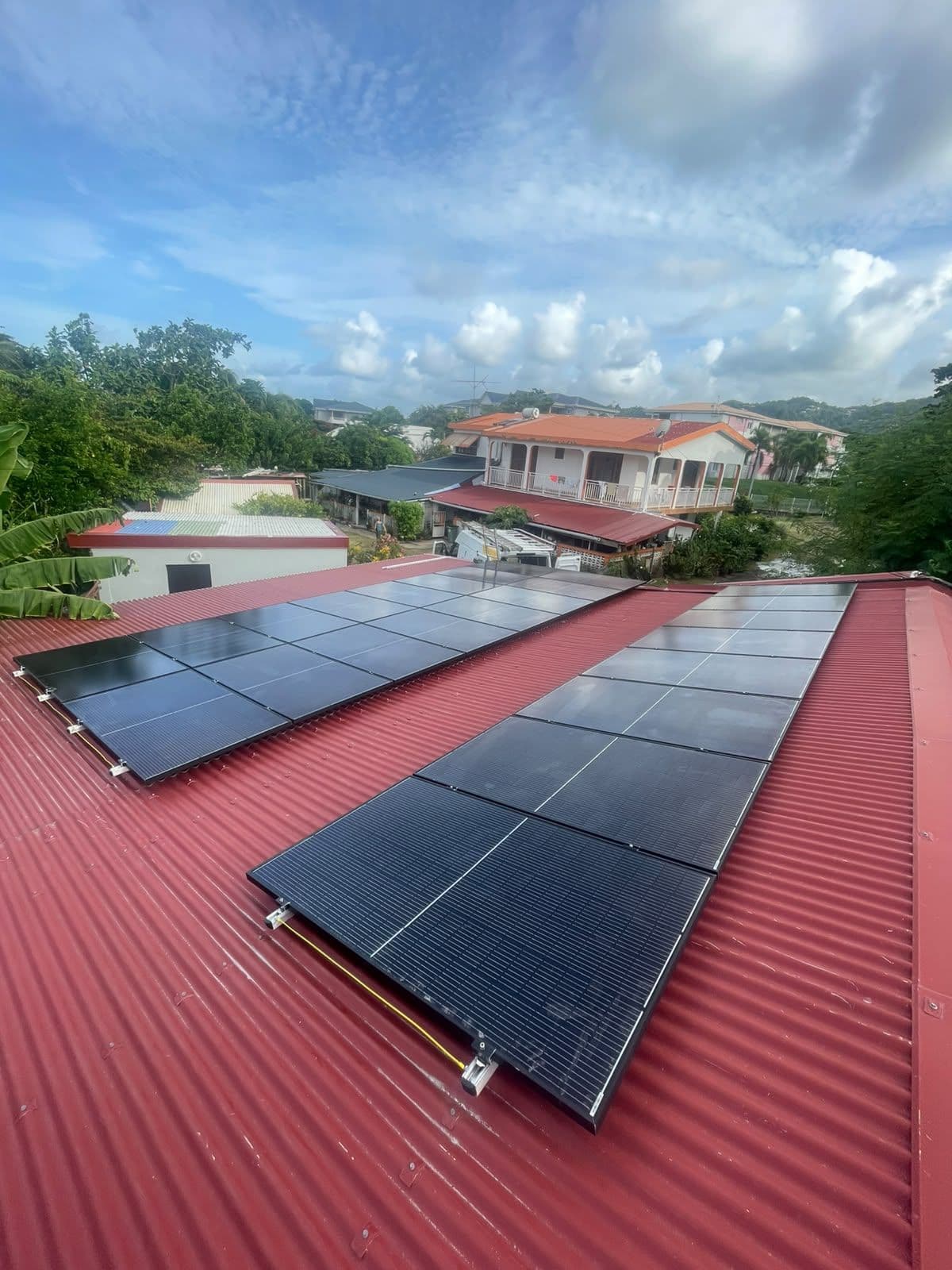 Deux champs de panneaux noirs sur une tôle rouge, maisons et mornes en fond